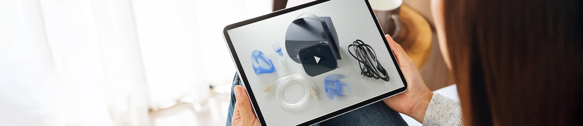 Blick über die Schulter einer braunhaarigen Frau. Sie blickt auf ein Tablet mit einemVideo zu einem medizinischen Gerät