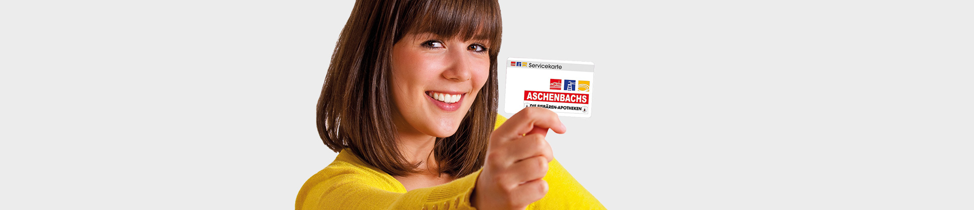 Eine junge lächelnde Frau mit dunklen Haaren in gelber Cardigan hält mit ausgestrecktem Arm eine Kundenkarte in die Kamera.