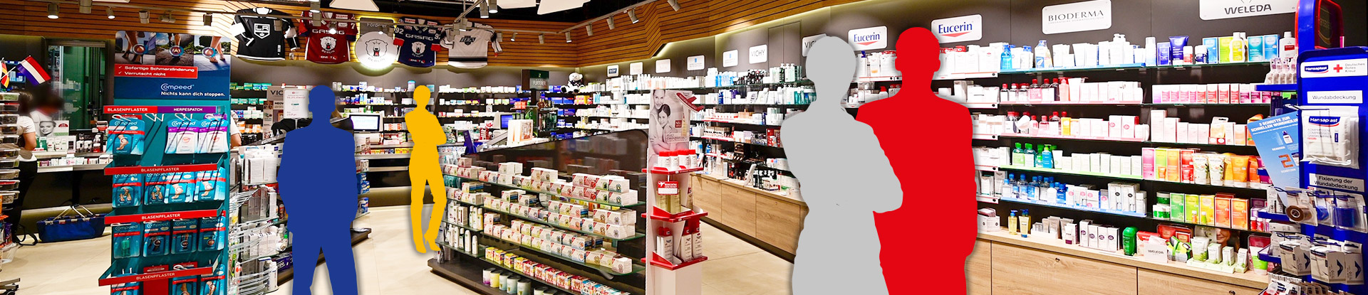 Innenansicht der Aschenbachs Arena Apotheke. Darauf montiert sind in 4 menschliche Silhouetten in blau, gelb, grau und rot.