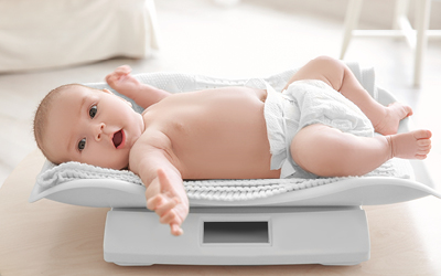 Ein Baby in Windel liegt mit einer Decke auf einer Babywaage